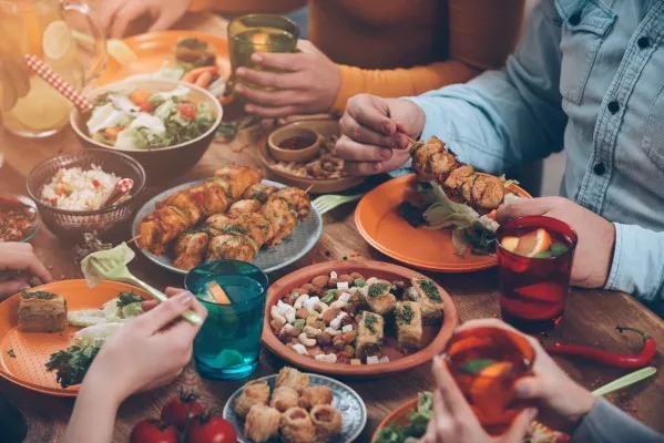 Family dinner with gourmet chicken skewers, vegetable salad, rice, seeds and nuts, and infusions to accompany on a wooden table.